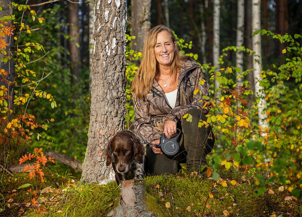 Anna sitter på huk i en färggrann lövskog tillsammans med sin hund